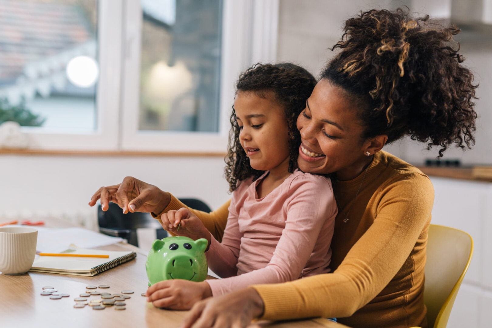Mother teaching daughter about money using coins and a piggy bank.