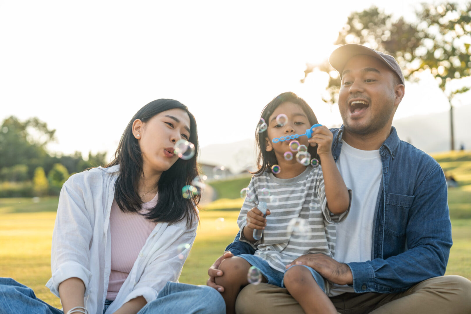 A joyful family blowing bubbles together outdoors on a sunny day.