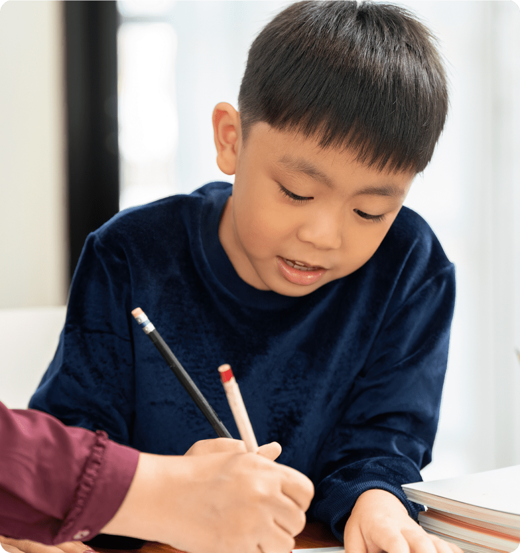 Child writing with adult's help at desk.